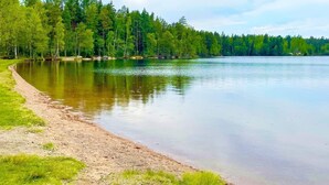 A calm lake with a sandy shore and dense forest in the background. - 8 Person Holiday Home in Hogsby (Högsby)