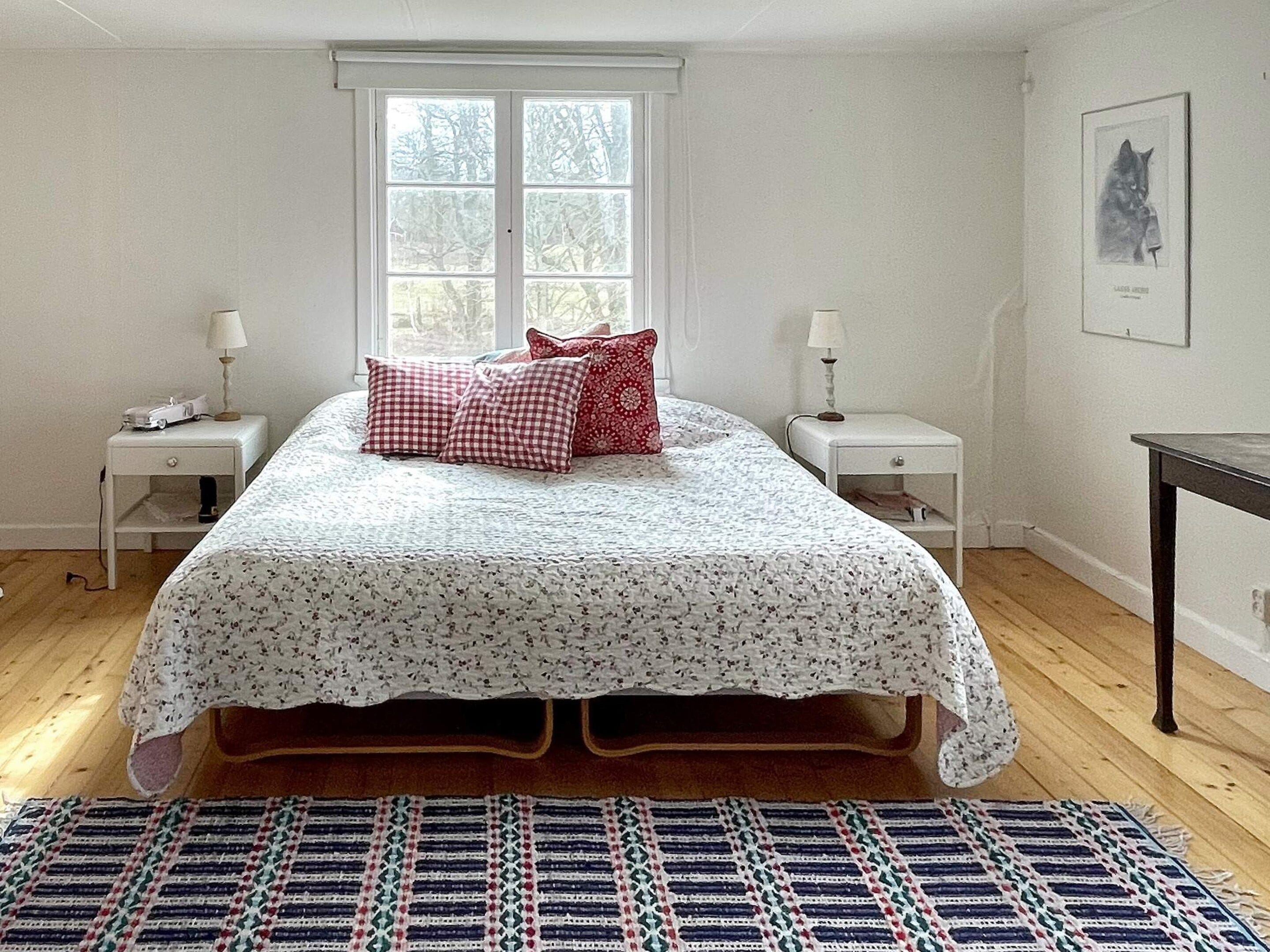A bedroom with a bed, two bedside tables, a window, and a framed picture on the wall.