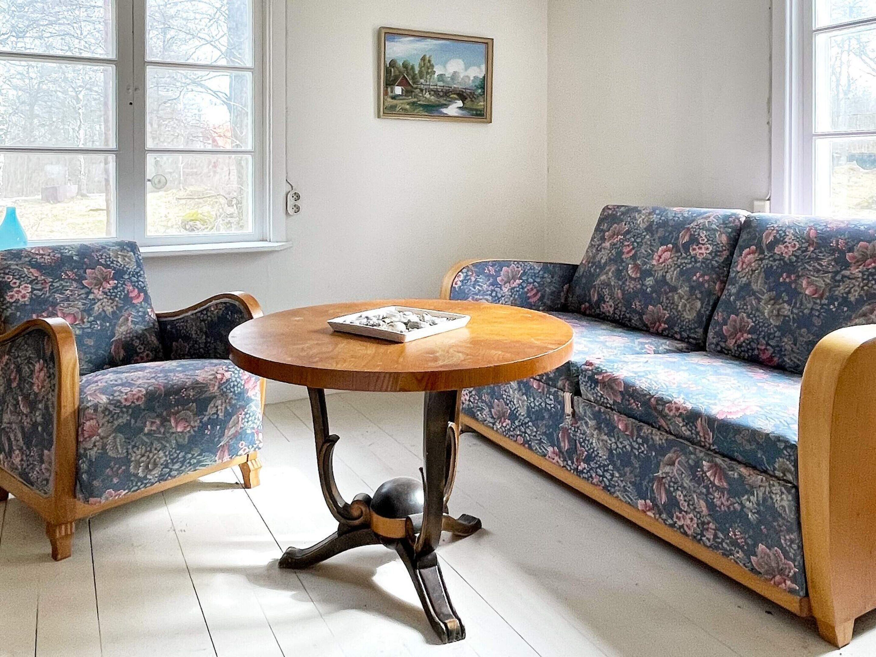 A room with a floral sofa, a round wooden table, and a painting on the wall.