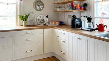 A kitchen with white cabinets, a wooden countertop, a coffee maker, a kettle, and a potted plant.