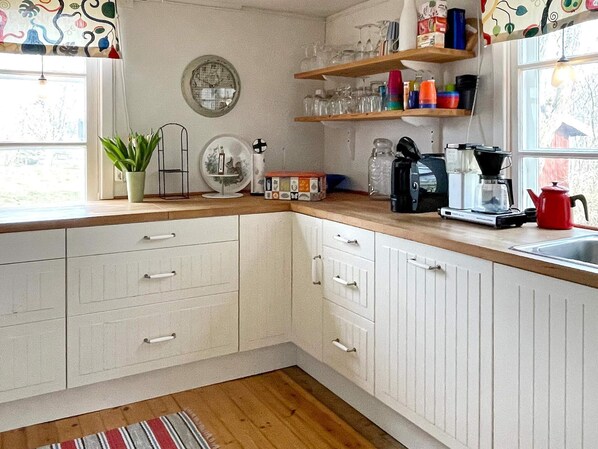 A kitchen with white cabinets, a wooden countertop, a coffee maker, a kettle, and a potted plant.