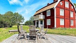 A red wooden house with a balcony, a wooden deck with chairs, and a clear blue sky. - 8 Person Holiday Home in Hogsby (Högsby)