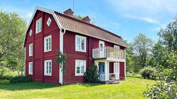 A two-story red house with a balcony, surrounded by greenery.