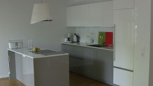 Eine moderne Küche mit weißen Schränken, einer zentralen Kochinsel, einer Kaffeemaschine und einem Kühlschrank.