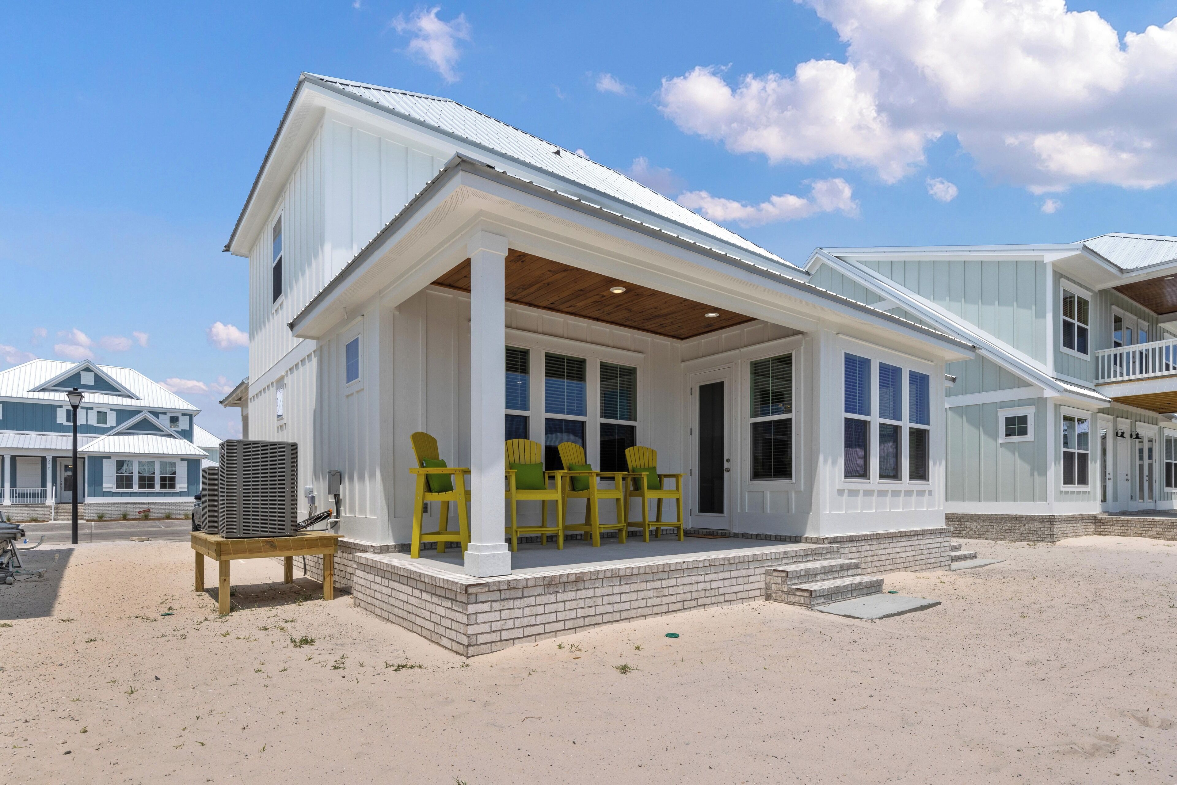 A beach house with a covered porch, outdoor seating, and a large air conditioning unit.