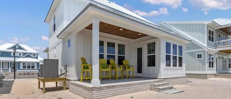 A beach house with a covered porch, outdoor seating, and a large air conditioning unit.
