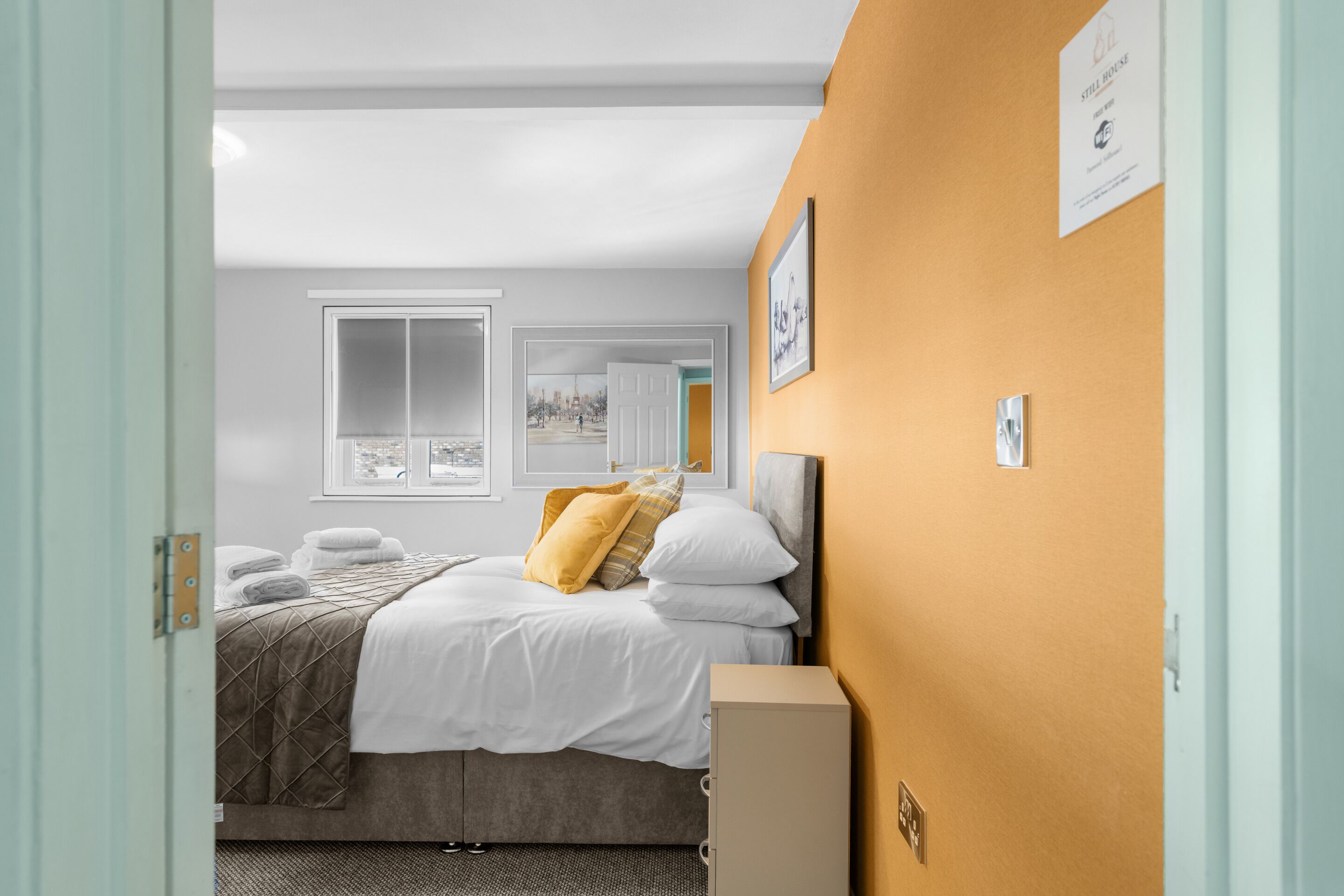 A hotel room with a bed, a cabinet, and a window with a view of a cityscape.