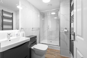 Un baño moderno con cabina de ducha de vidrio, un lavabo blanco y un mueble de tocador de tonos oscuros.