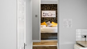 Un pasillo estrecho que lleva a un dormitorio con cama, una escalera de madera y un área de lavandería.