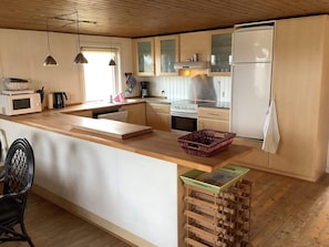 A modern kitchen with wooden cabinets, a central island, a microwave, a stove, and a refrigerator. - 6 Person Holiday Home in Thisted (Thisted)