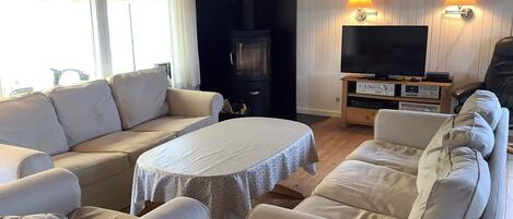 A cozy living room with a sofa set, a round table, a TV, and a wood-burning stove.