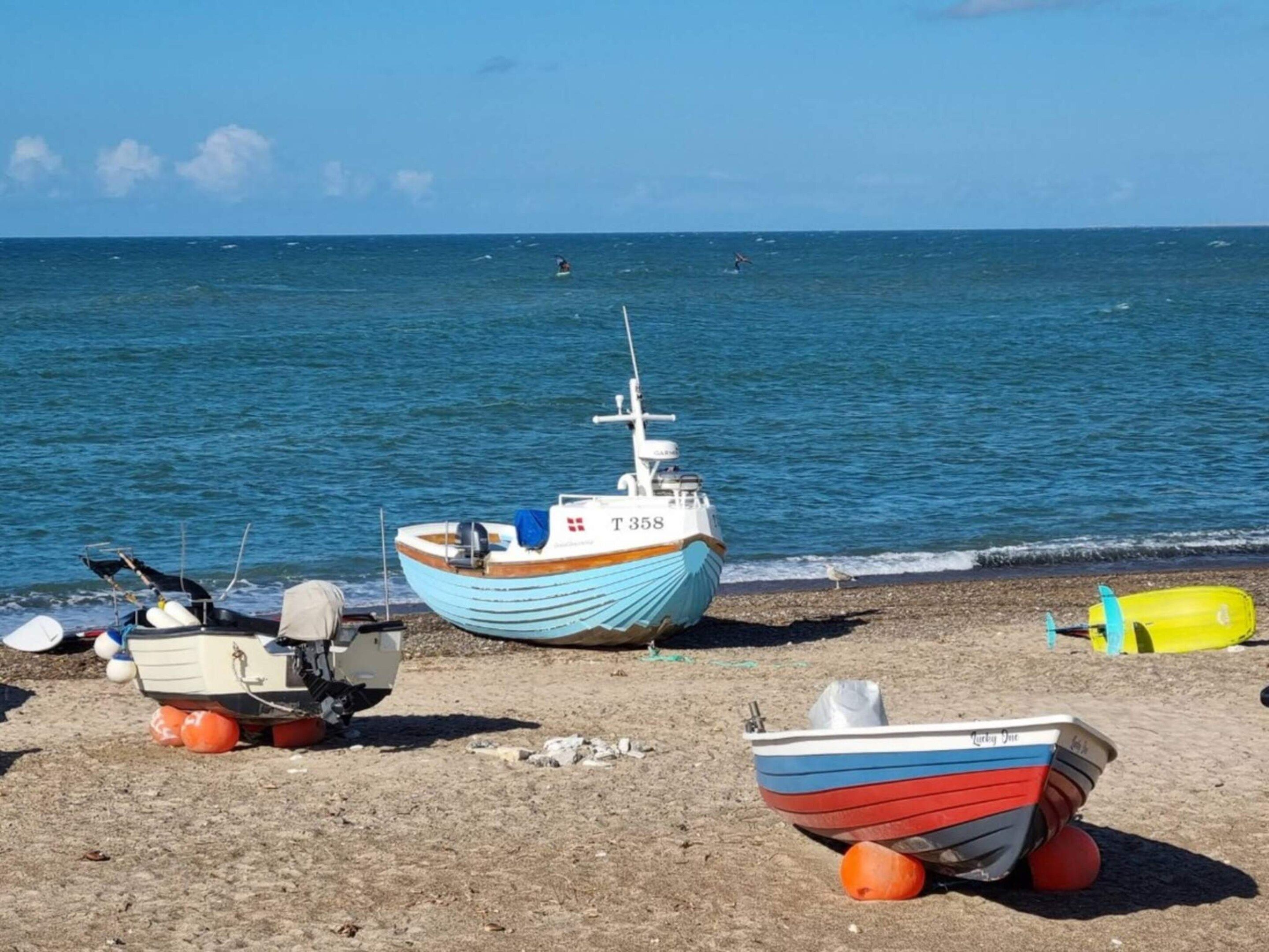 Una playa con varios barcos, incluyendo uno azul y blanco con el número T358, y un bote más pequeño rojo y blanco.