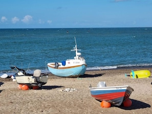 A beach with several boats, including a blue and white one with the number T358, and a smaller red and white boat.