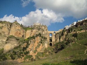 A historic stone bridge with arches, a building on top, and a path leading up the hill. - Watervallen van de Zon 1 (Mijas)
