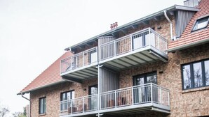 A two-story building with a brick facade, a balcony with metal railings, and a paved walkway leading to the entrance. - Narrow Luzin Modern Retreat (Feldberger Seenlandschaft)