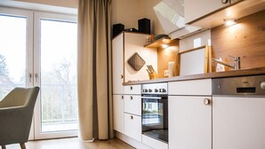 A modern kitchen with a built-in oven, a dining area with a chair, and a sliding glass door leading to a balcony. - Narrow Luzin Modern Retreat (Feldberger Seenlandschaft)