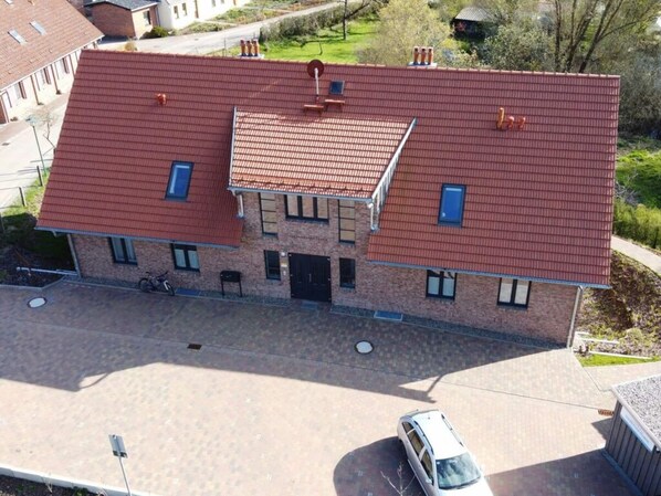 A two-story building with a red-tiled roof, a central entrance, and a small parking area.