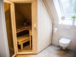 A sauna room with wooden walls and a bench, a toilet, and a window with a plant.