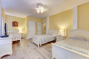 Quarto com duas camas, uma escrivaninha, um guarda-roupa e um ventilador de teto.