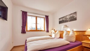 A bedroom with a bed, wooden headboard, a window with curtains, a wall-mounted TV, and a painting. - "karwendel" Modern Retreat (Kruen)