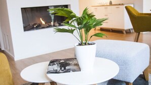 Una sala de estar moderna con una mesa redonda blanca, una planta en maceta, una revista, un sofá y una chimenea.