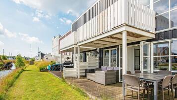 A modern house with a covered patio, outdoor seating, and a view of a canal.