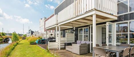 A modern house with a covered patio, outdoor seating, and a view of a canal.