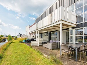 Una casa moderna con un porche cubierto, mobiliario exterior y vistas a un canal.
