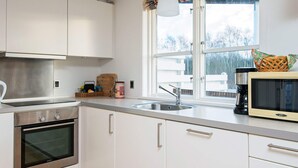 Una cocina moderna con armarios blancos, electrodomésticos de acero inoxidable, un ventanal con vistas y un microondas en la encimera.