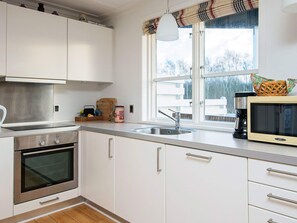 Una cocina moderna con armarios blancos, electrodomésticos de acero inoxidable, un ventanal con vistas y un microondas en la encimera.