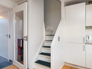 Una escalera de paredes blancas y piso de madera que conduce a una plataforma con un armario blanco y una tetera.