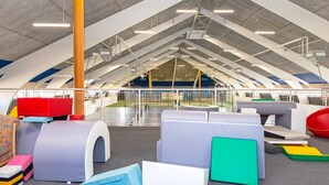 Un espacio de juegos interior con asientos acolchados y vistas a un campo deportivo exterior.