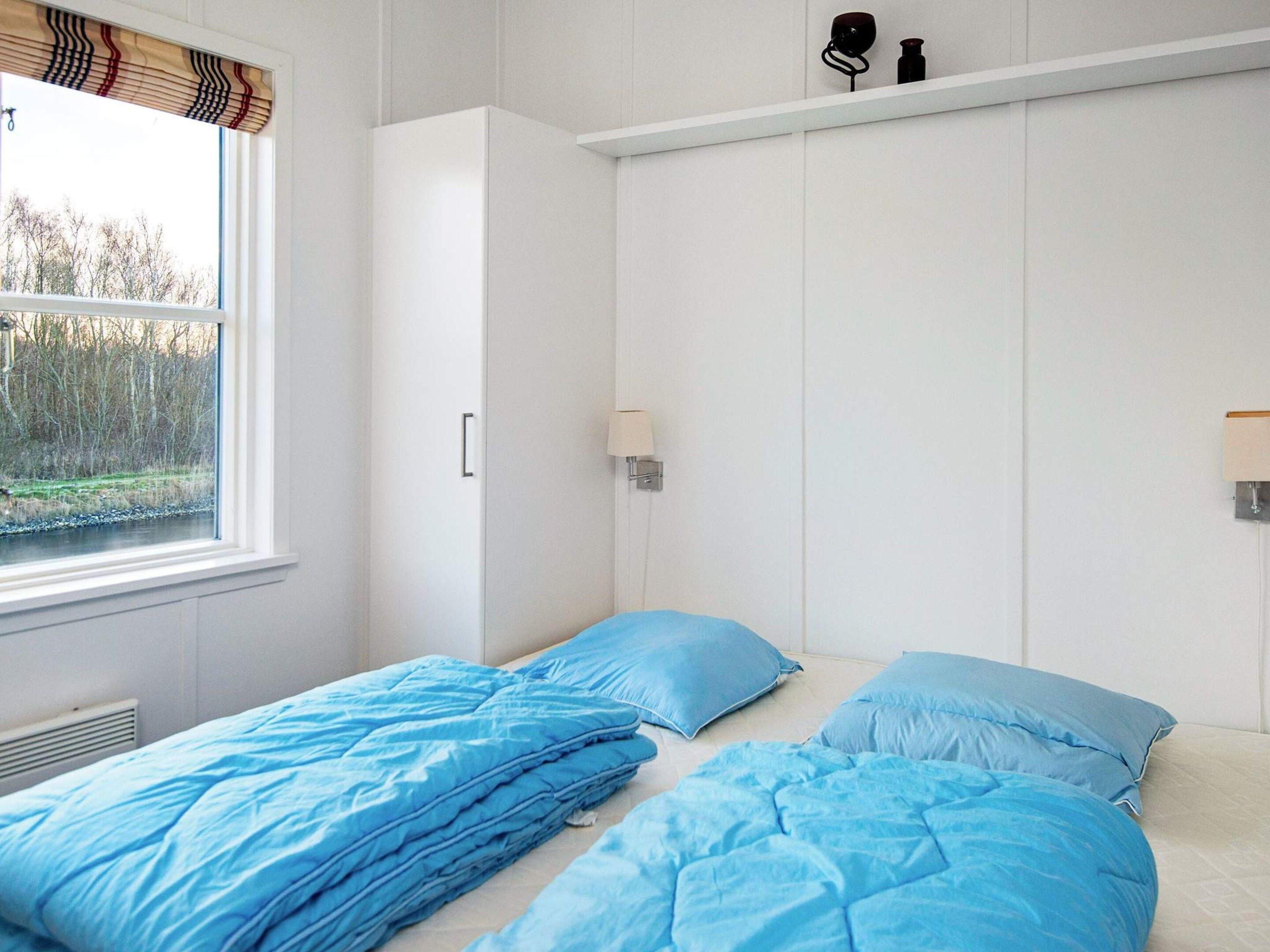 A bedroom with two beds, a window with a view of trees, a white wardrobe, and a shelf with items.