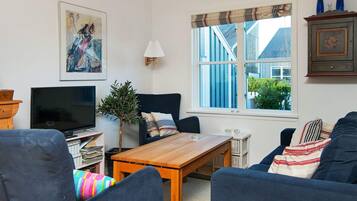 Un salón con televisor, sofá, mesa y ventana con vistas a edificios.