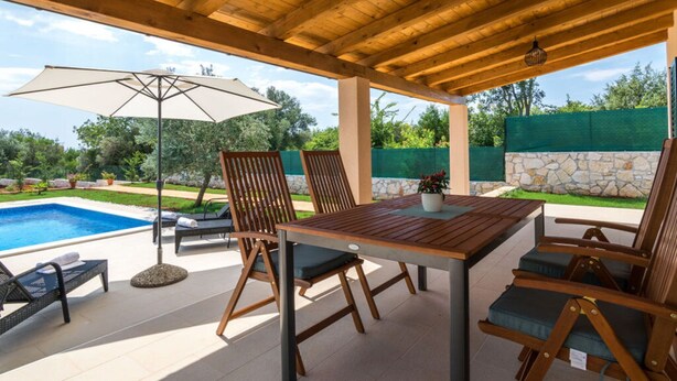 Eine Außenpatio mit Holztisch und -stühlen, einem Pool und Blick ins grüne Umland.
