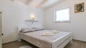 Ein Schlafzimmer mit einem Bett, einem Nachttisch, einem Fenster und einem Wandregal mit einer Lampe.