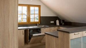 A modern kitchen with wooden cabinets, a dishwasher, and a large window offering a view of the outdoors.