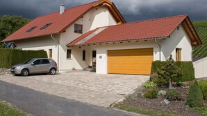 A two-story house with a red-tiled roof, a car parked in the driveway, and a well-maintained garden.