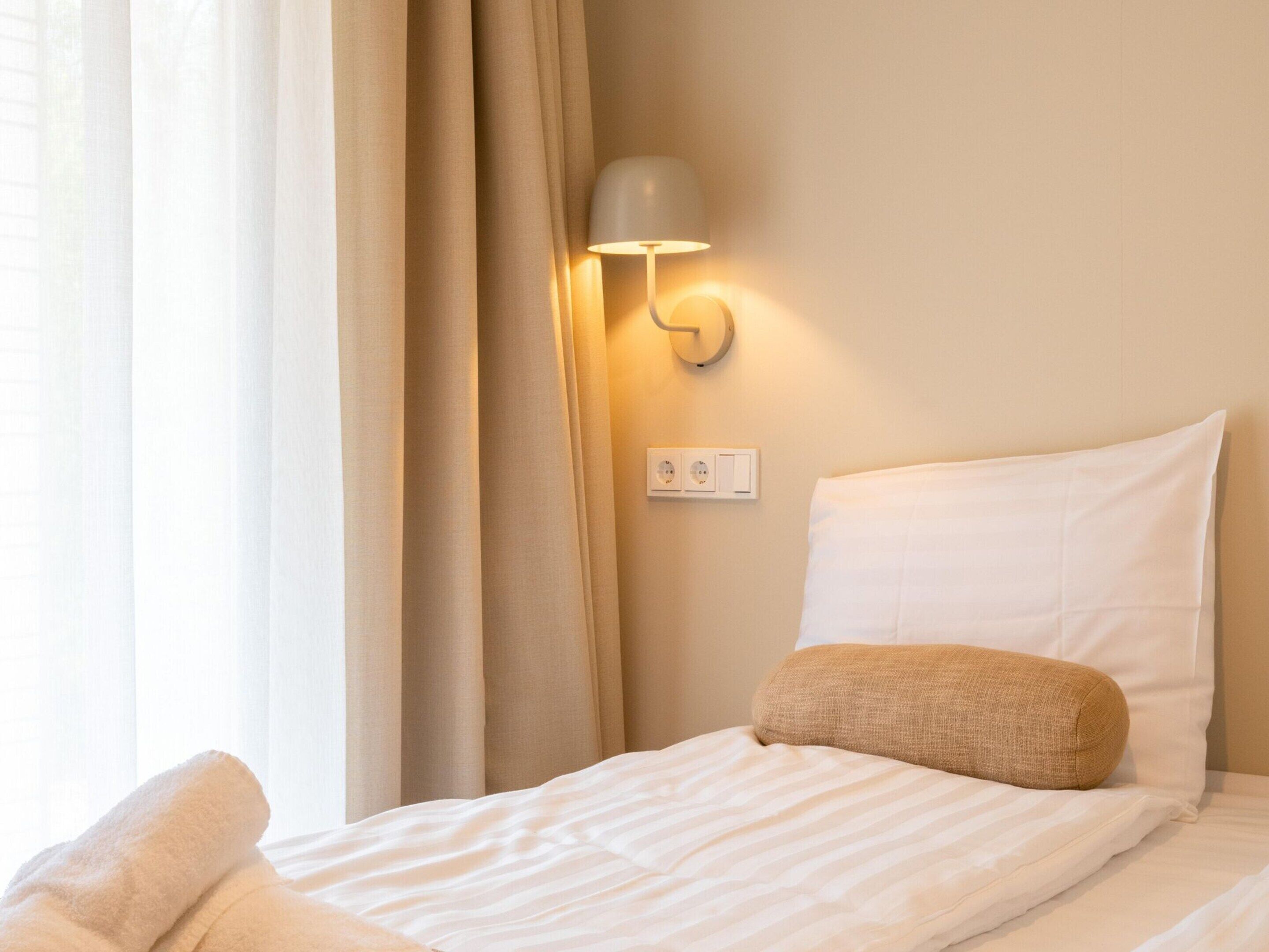 A hotel room with a neatly made bed, a wall-mounted lamp, and a power outlet.