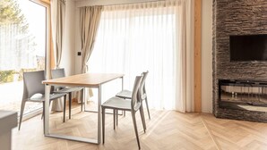Un soggiorno moderno con un tavolo da pranzo in legno, sedie grigie, un camino in pietra e ampie finestre con tende leggere.
