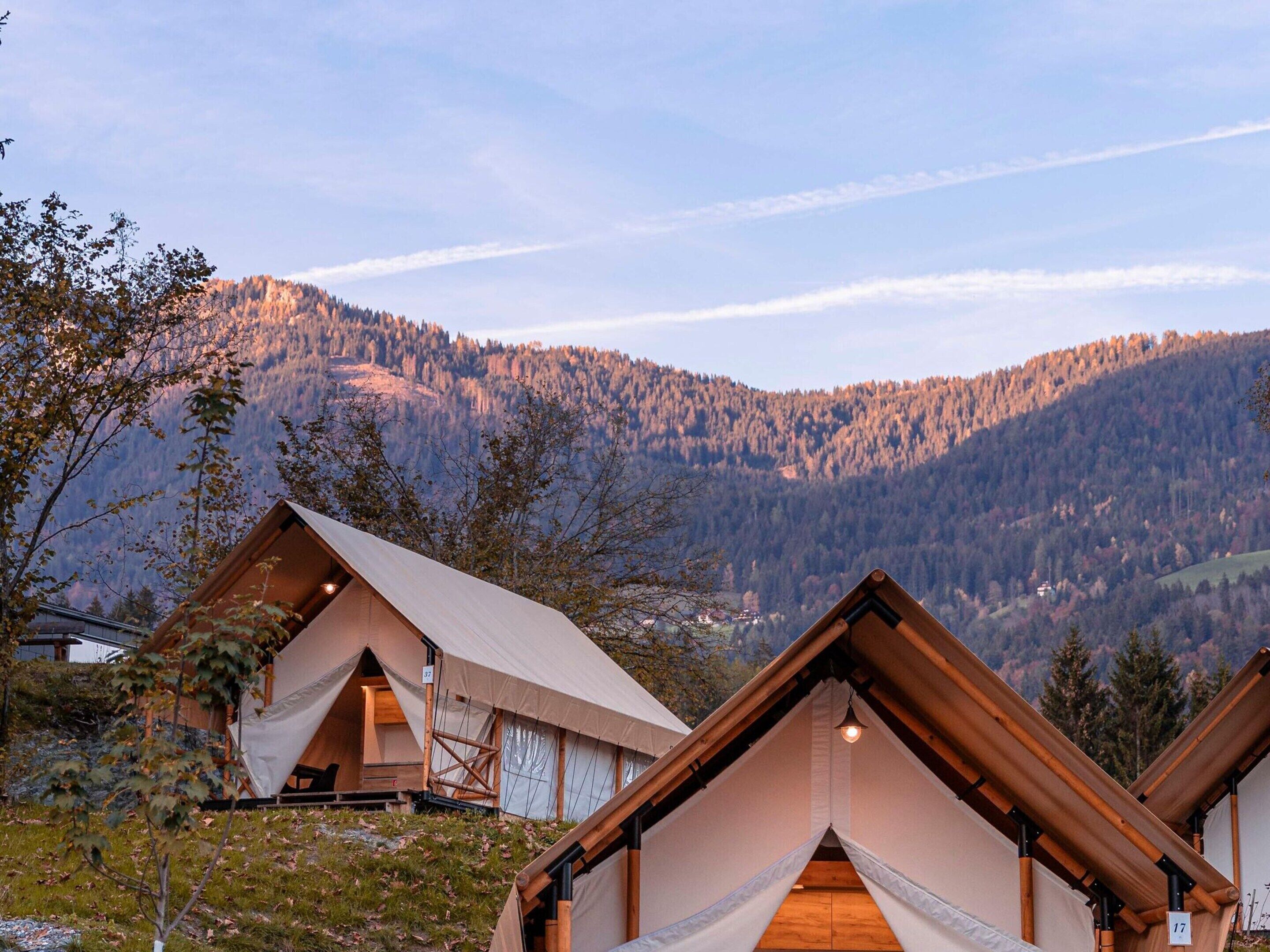 Une série de chalets en bois aux toits en pente, situés au pied d’une chaîne de montagnes boisées.