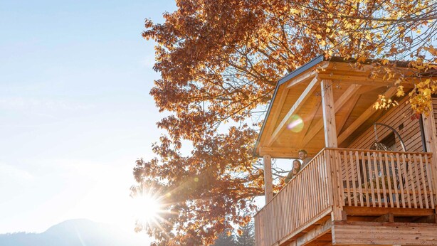 Una baita di legno con un balcone, circondata da autunno e montagne sullo sfondo.