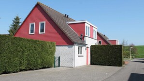A red two-story house with a grey roof, white brick lower section, and a green gate. - Nice Holiday Home With Garden Near Beach (Wemeldinge)