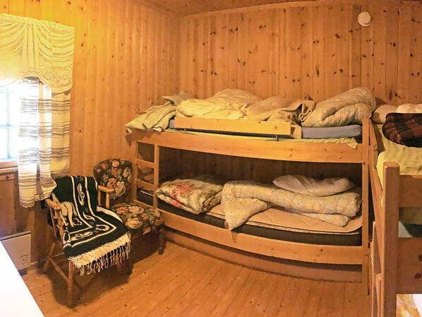 Habitación con literas, paredes de madera y un sillón estampado con flores.