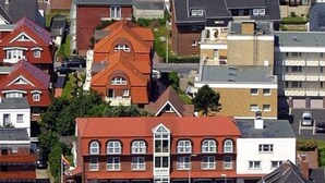 En byggnad med flera våningar, ett rött tak, en skylt med texten ”HOPPE” och en parkeringsplats framför.