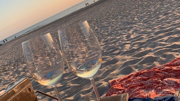 Två tomma vinglas på en strand, tillsammans med en filt och en trälåda.