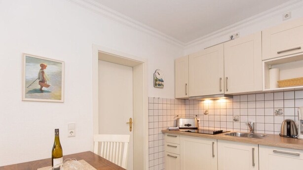 Une cuisine de taille réduite, avec des meubles blancs, une table en bois et un tableau accroché au mur.