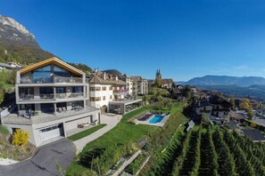 A modern two-story house with a large balcony, a swimming pool, and a view of a church and mountains. - Apartment Pink Lady 1 (Caldaro Sulla Strada del Vino)