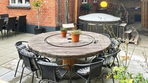 A round wooden table with chairs, potted plants, and a hot tub in a backyard with a brick wall and wooden fence. - 5 Star Holiday Home in Grindsted (Grindsted)