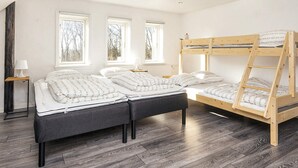 Une chambre avec un lit superposé, deux tables de chevet et une fenêtre donnant sur les arbres.
